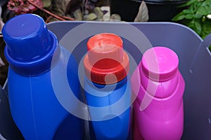 Three empty colored containers for detergent inside a gray basket. Recycling concept of plastic waste