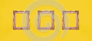 three empty ornate gold picture frames on yellow wall background