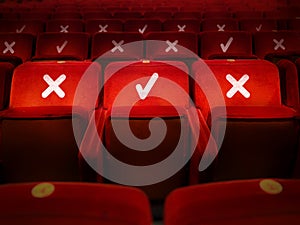 Three empty red velvet armchairs illuminated inside a concert hall