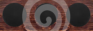 Three empty rustic black slate plates on wooden brown textured background, top view