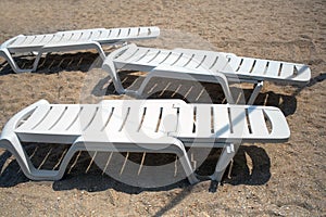 Three empty white plastic deck chairs chaise lounges at sandy beach during sunny day top view