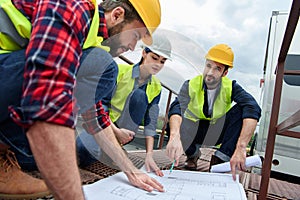 three engineers in hardhats working with blueprints