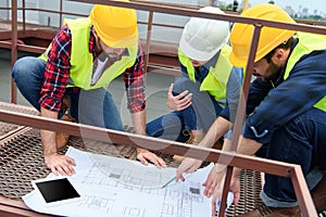 three engineers in safety vests and hardhats working with blueprints