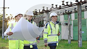 Three engineers walk near power lines in the high voltage power station. Power specialists are planning a new project