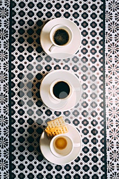 Three espresso coffee cups and saucers on pattern table cloth
