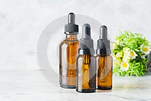 three essential oil dropper bottles with chamomile flowers out of focus in the background