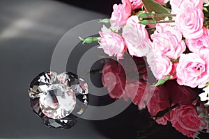 Three excellent diamonds of the first water and bouquet of pink roses with reflection on black mirror background close up view.