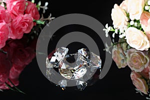 Three excellent diamonds of the first water and bouquets of pink and tea roses with reflection on black mirror background close up