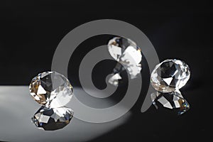 Three excellent pure diamonds with reflection on black mirror background close up view selective focus. Jewelry diamonds sale,