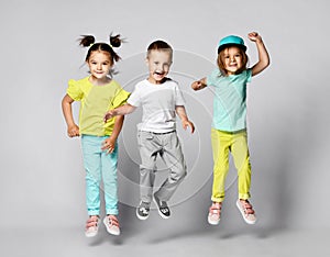 Three excited kids in fashion outfits, jumping over the light background. Two sisters and brother, friends in fashionable clothes