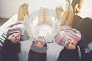 Three excited teenager girls having fun together enjoying laze leisure time on bed