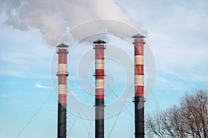 Three factory chimneys emit puffs of smoke against the blue sky.