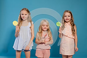 Three fashionable little girls eat candy lollipop