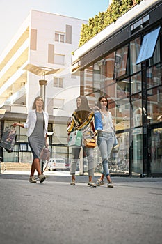 Three fashionable young women strolling with shopping bags. Women walking on street.