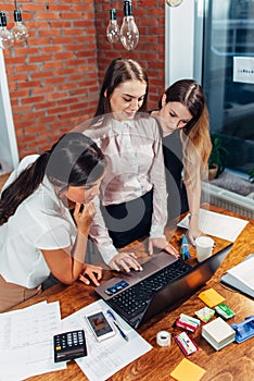 Three female college students working on assignment together using laptop standing at home