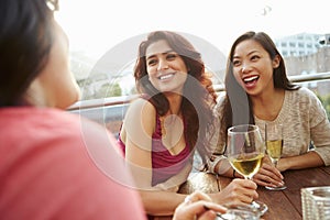 Three Female Friends Enjoying Drink At Outdoor Rooftop Bar