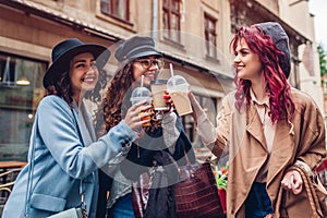 Three female friends having drinks outdoors. Women clinking coffee, orange juice and tea cups