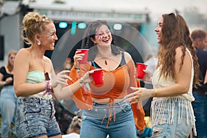 Three Female Friends Wearing Glitter Dancing At Summer Music Festival Holding Drinks