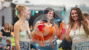 Three Female Friends Wearing Glitter Dancing At Summer Music Festival Holding Drinks