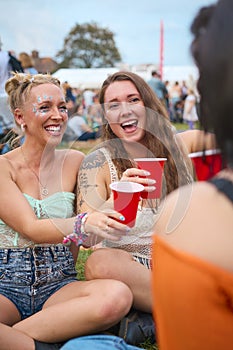 Three Female Friends Wearing Glitter Having Fun At Summer Music Festival Doing Cheers With Drinks