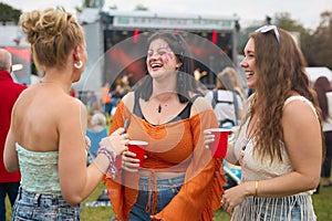 Three Female Friends Wearing Glitter Having Fun At Summer Music Festival Holding Drinks