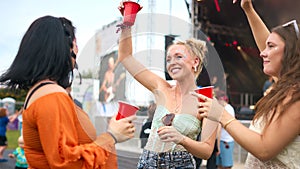 Three Female Friends Wearing Glitter Having Fun At Summer Music Festival Holding Drinks