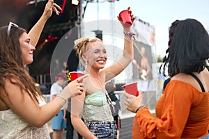 Three Female Friends Wearing Glitter Having Fun At Summer Music Festival Holding Drinks
