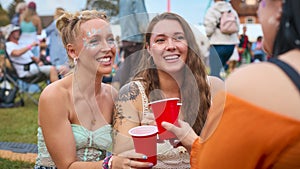 Three Female Friends Wearing Glitter Having Fun At Summer Music Festival Holding Drinks