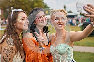 Three Female Friends Wearing Glitter Posing For Selfie At Summer Music Festival 