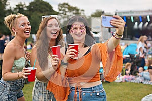 Three Female Friends Wearing Glitter Posing For Selfie At Summer Music Festival Holding Drinks