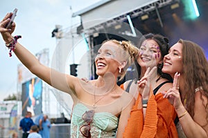 Three Female Friends Wearing Glitter Posing For Selfie At Summer Music Festival Holding Drinks
