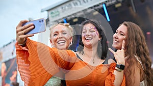 Three Female Friends Wearing Glitter Posing For Selfie At Summer Music Festival Holding Drinks