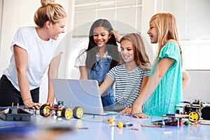 Three Female Students With Teacher Building Robot Vehicle In After School Computer Coding Class