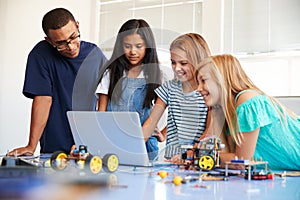 Three Female Students With Teacher Building Robot Vehicle In After School Computer Coding Class