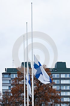Three finnish flags lowered to half mast on the occasion of mourning at cloudy autumn day