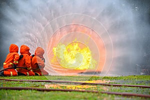 Three firefighters water spray with high pressure to fire surround with water drops and smoke.