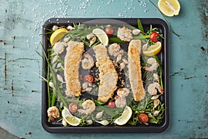 Three fishfingers and shrimps with vegetables on the baking tray