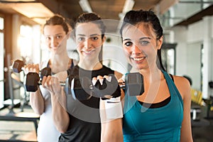 Three fit and beautiful young women lifting weights in a fitness club. Focus on the first girl in front