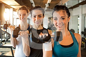 Three fit and beautiful young women lifting weights in a fitness club. Focus on girl in the center