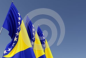 Three flags of Bosnia and Herzegovina on flagpole on blue background. Place for text. The flag is unfurling in wind. Europe,