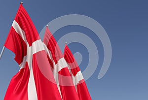 Three flags of Denmark on a flagpole on a blue background. Place for text. The flag is unfurling in wind. Danish. Europe,