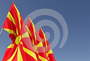 Three flags of Northern Macedonia on a flagpole on a blue background. Place for text. The flag is unfurling in wind. Europe,