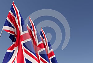 Three flags of the United Kingdom on a flagpole on a blue background. Place for text. The flag is unfurling in wind. Great Britain