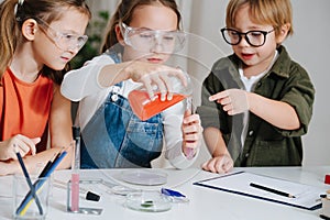 Three focused little kids doing home science project, filling the flask