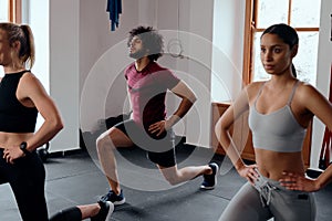 Three focused multiracial young adults in sportswear doing lunges at the gym