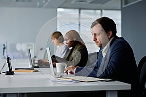 Three focused young multiracial business people in businesswear working at desk on laptops in office