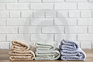 Three folded bath towels on wooden table and white brick wall on background. Beige, lavender and mint colors