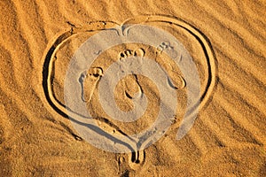 Three footprint and heart on sand