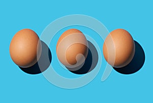 Three fresh brown eggs lie side by side on a blue background
