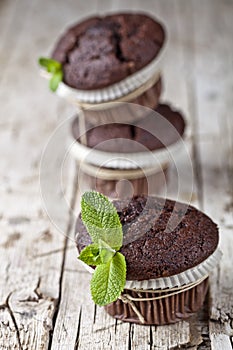 Three fresh dark chocolate muffins with mint leaves on rustic wooden table